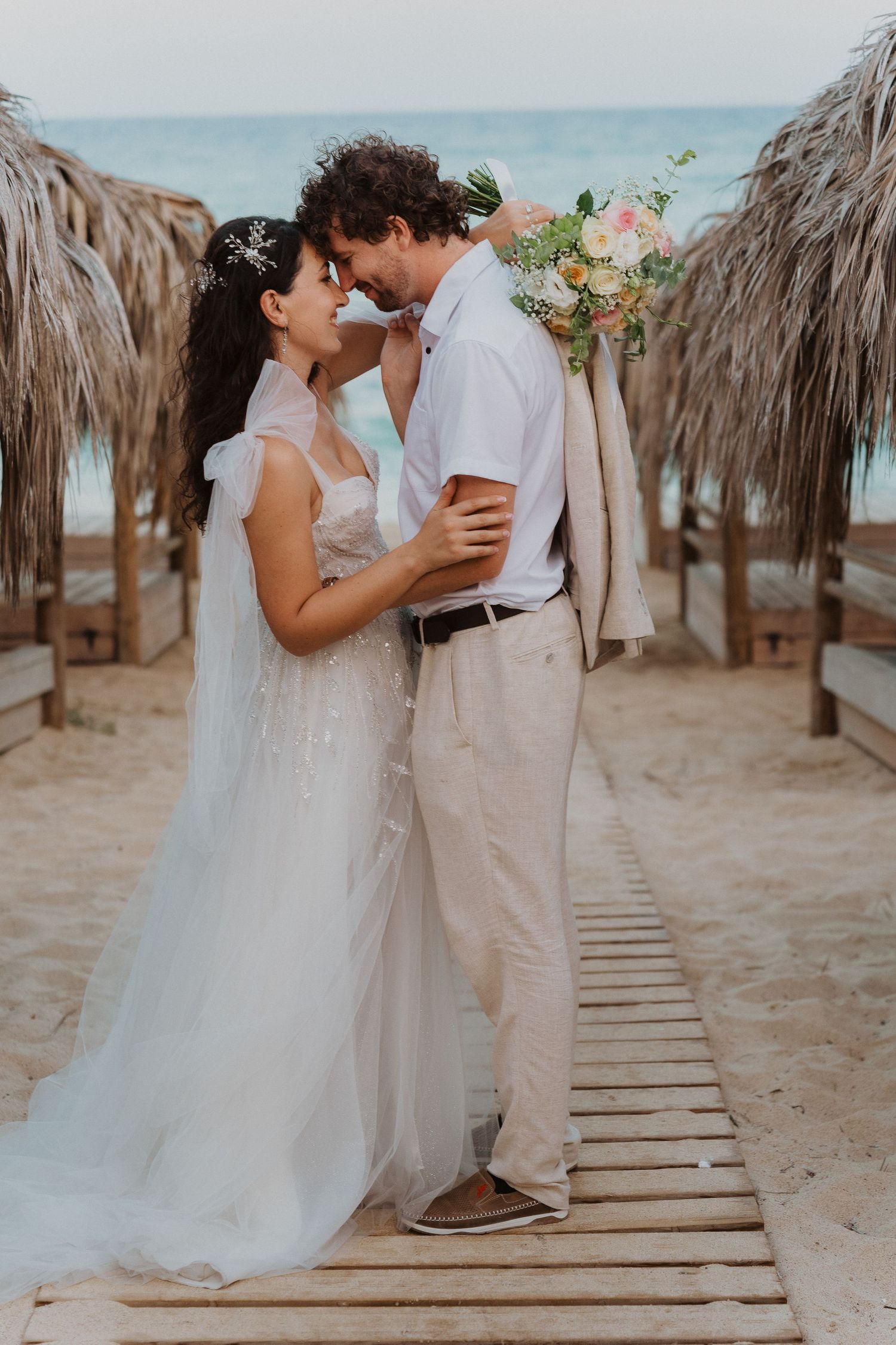 Romantic moment captured between couple at beach wedding with thatched umbrellas.