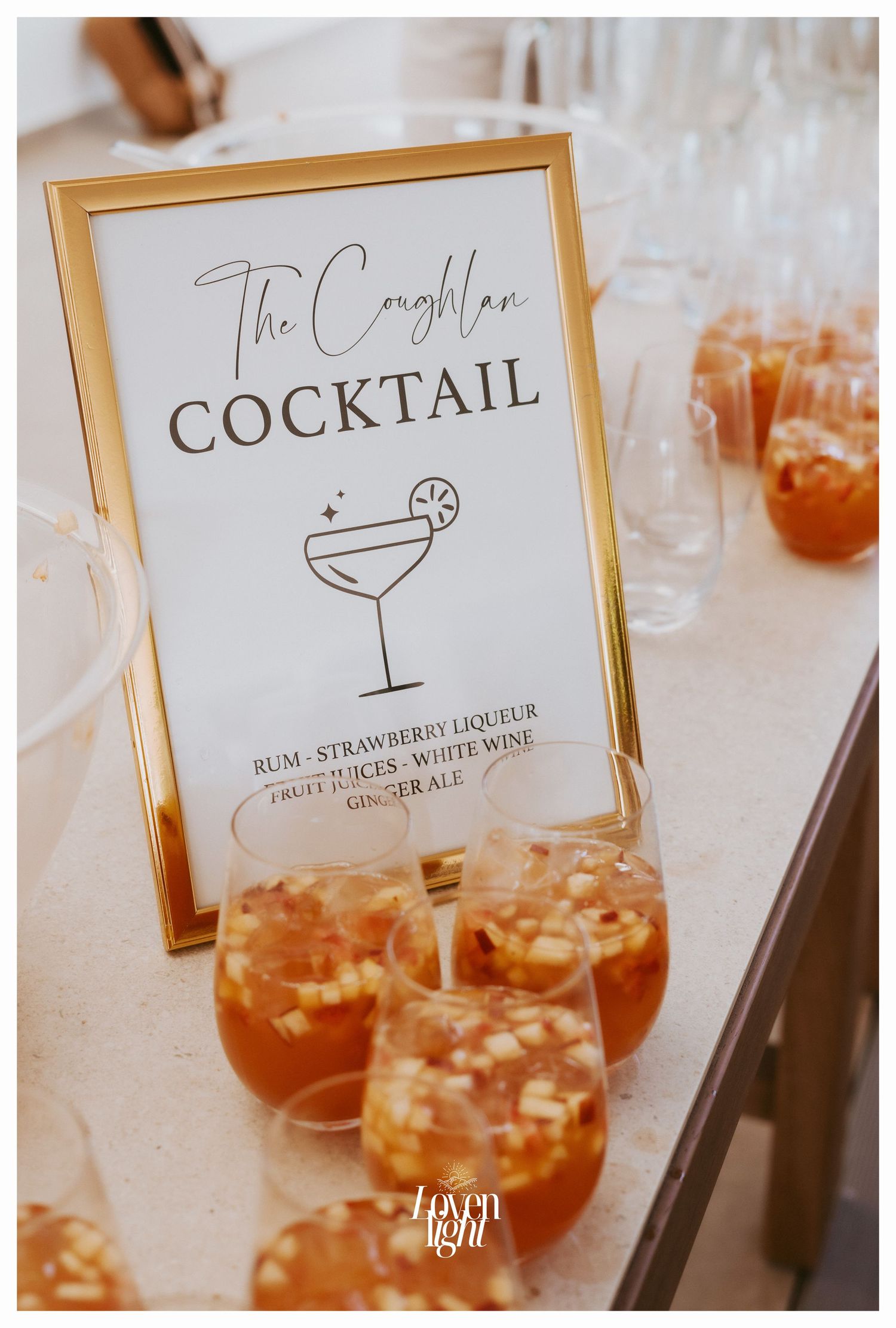 Wedding cocktail menu in a gold frame with signature drinks displayed on a white table.