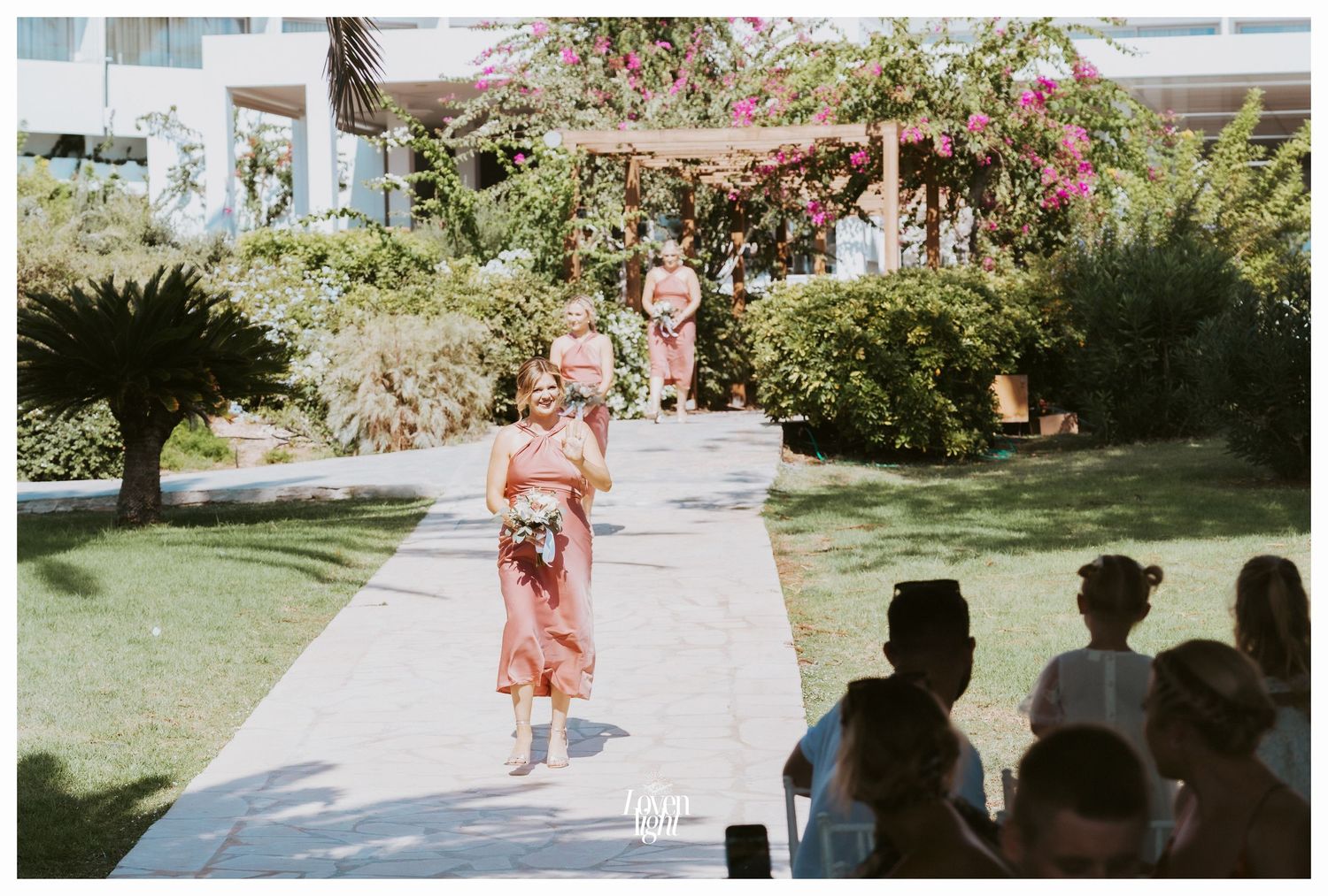 Wedding processional on garden path with pink bougainvillea flowers overhead.