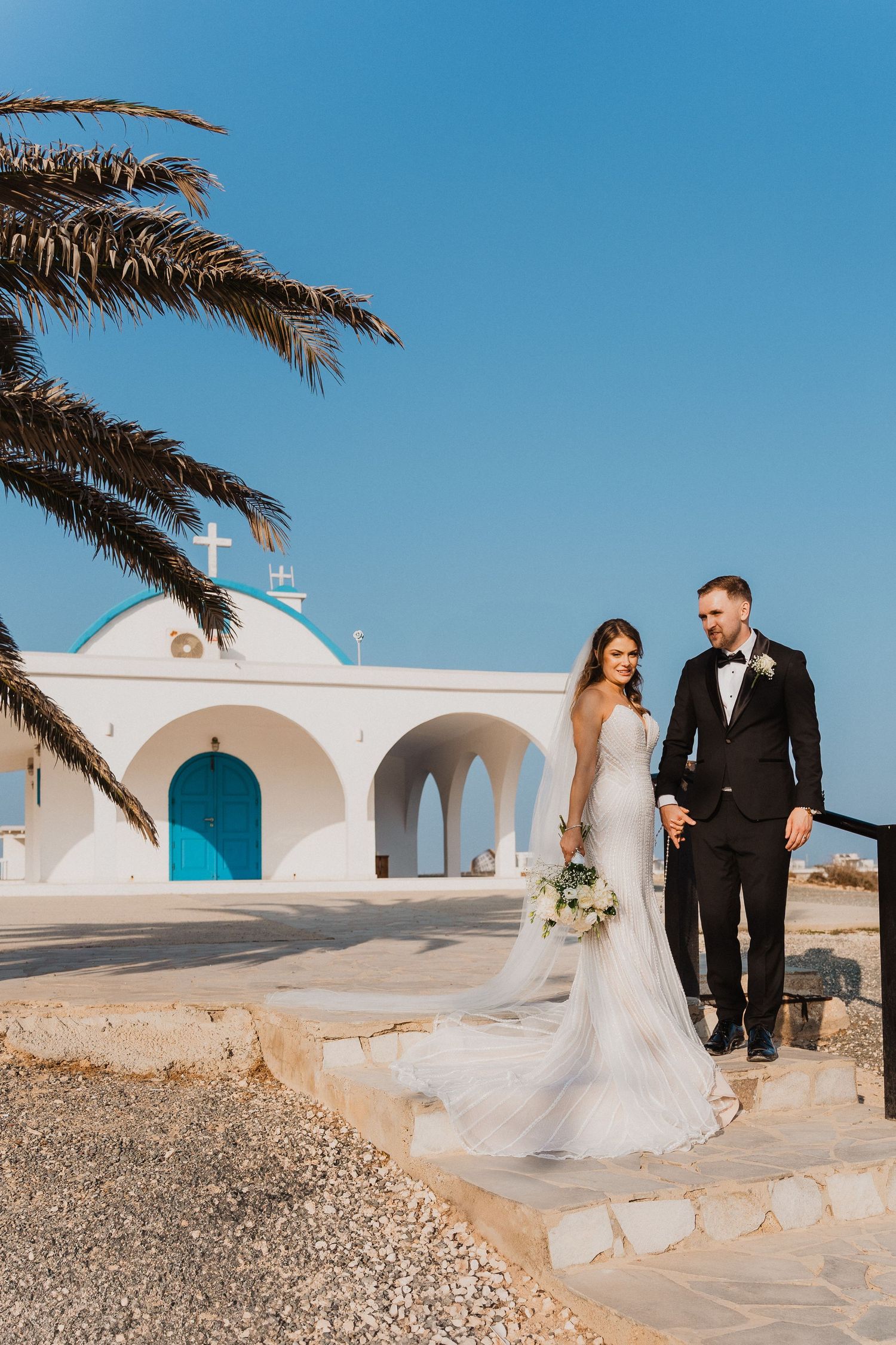 Mediterranean wedding venue with white arches and palm trees creates stunning backdrop.