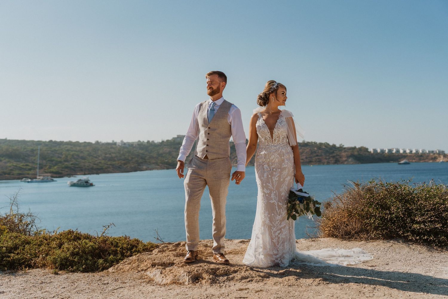 Couple in wedding attire exploring rocky coastal viewpoint.