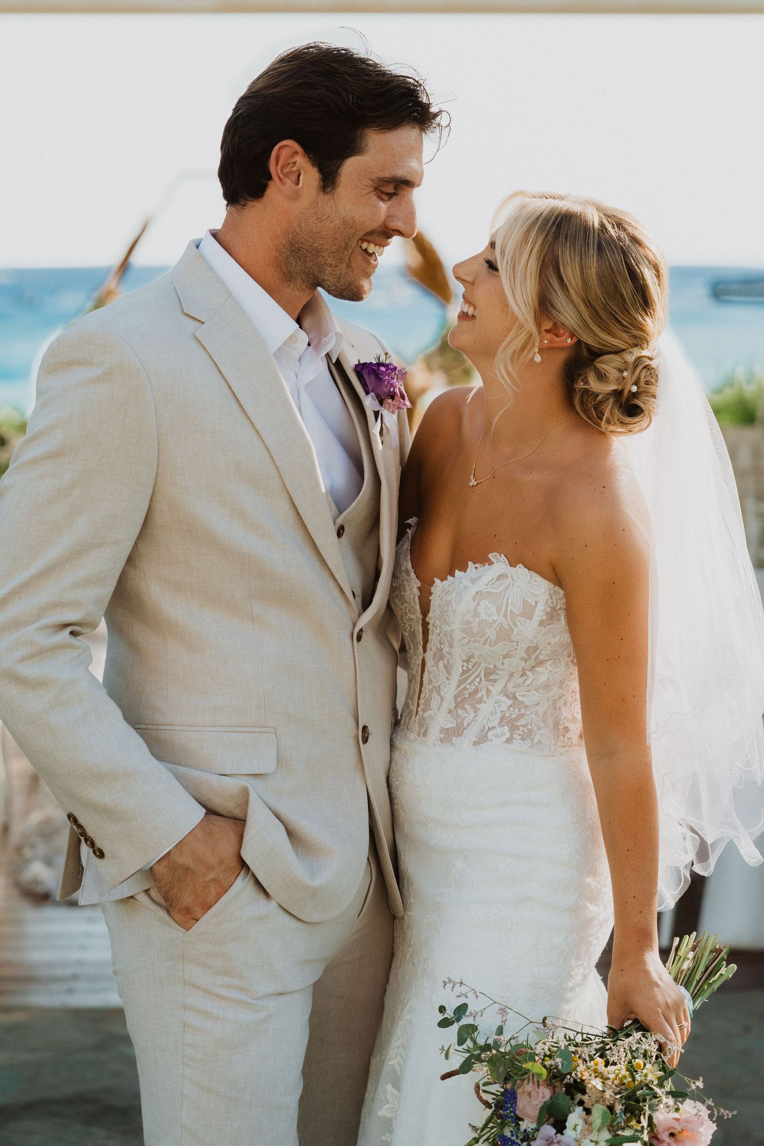 A candid wedding moment shared between newlyweds with the ocean visible in the background.