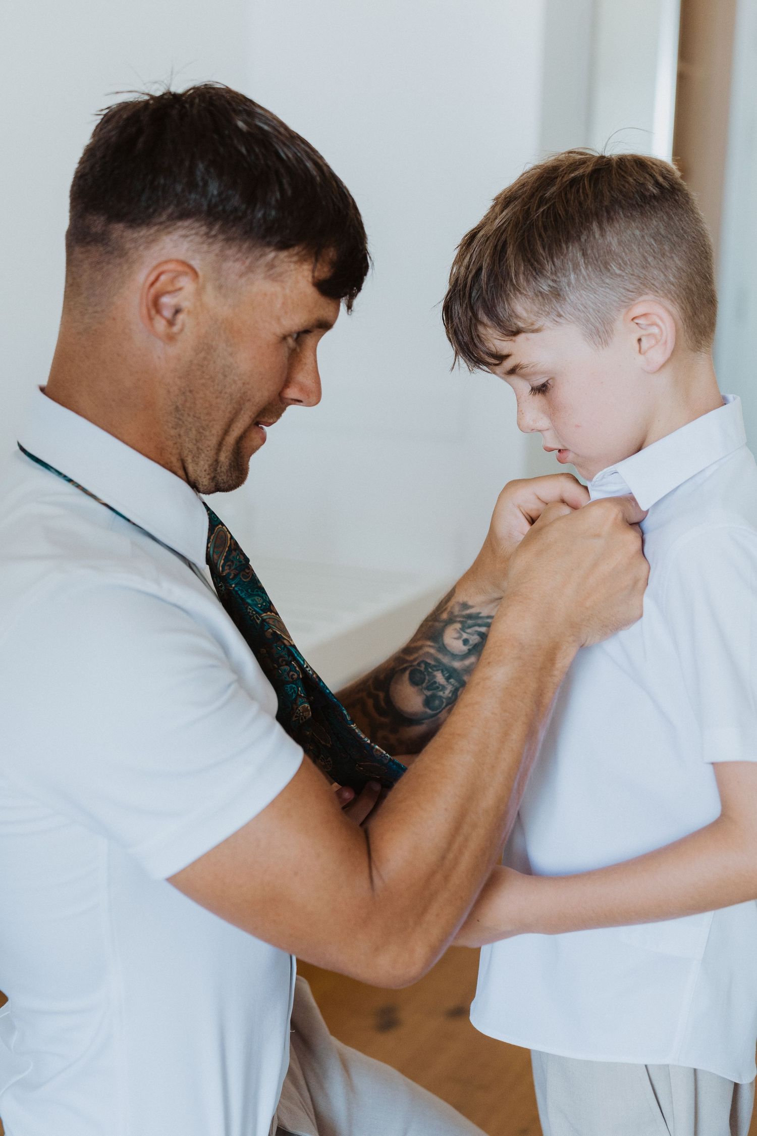 A caring moment shows an adult helping a child fix the collar of their white dress shirt while wearing a tie.