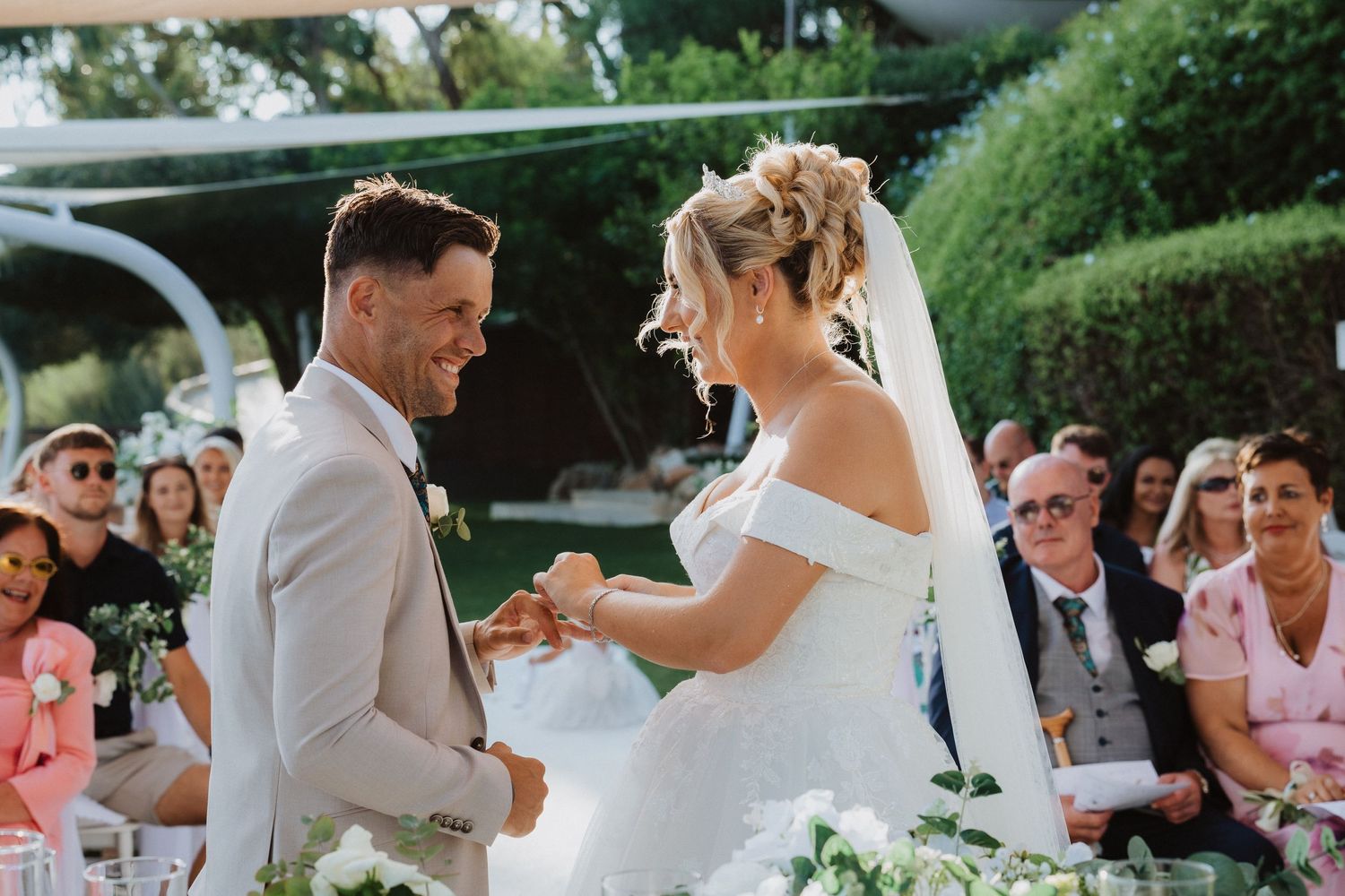 Joyful wedding ceremony moment under a canopy with guests watching the exchanging of vows.