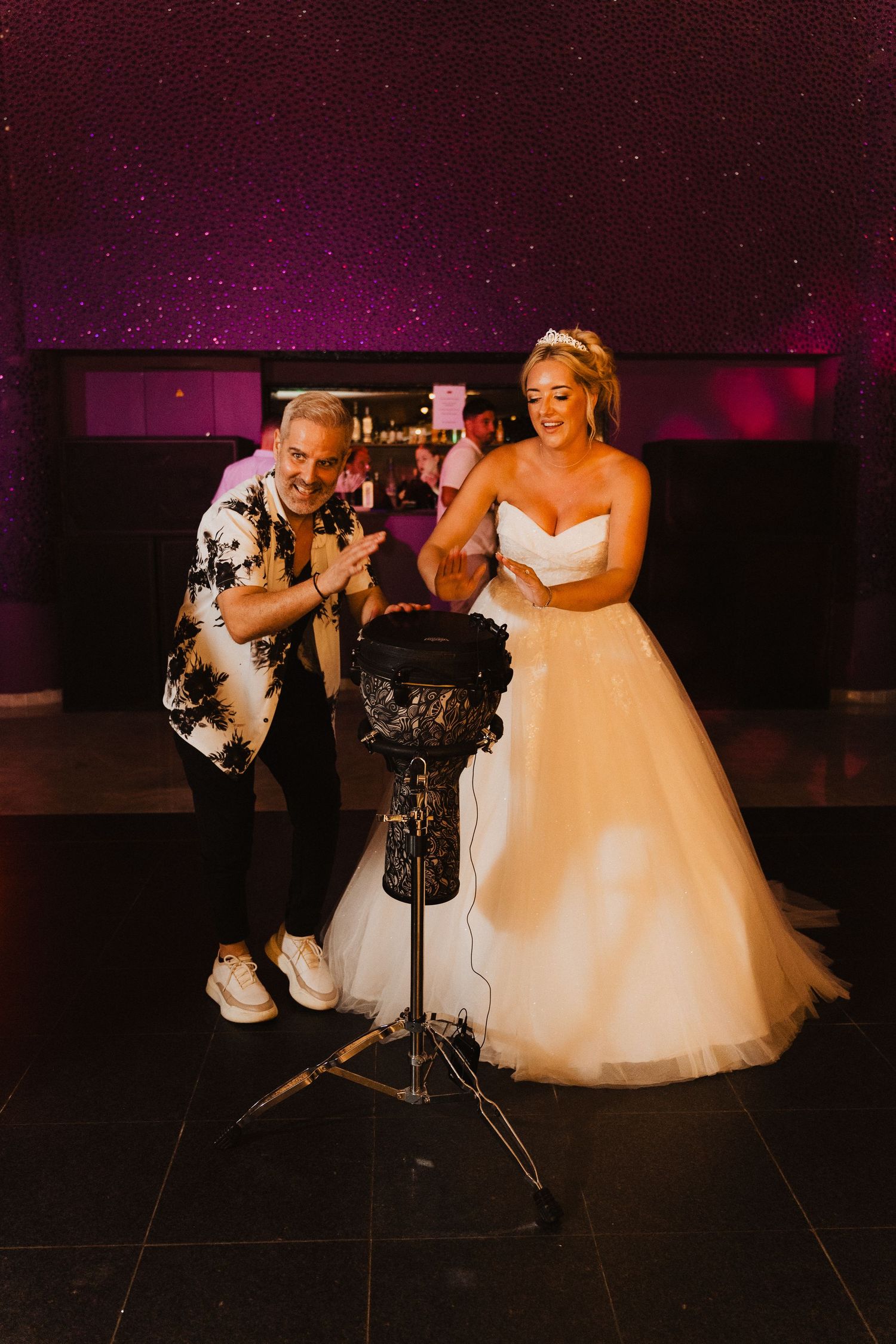 Wedding celebration scene with karaoke entertainment on a dark stage with purple lighting and a formal atmosphere.