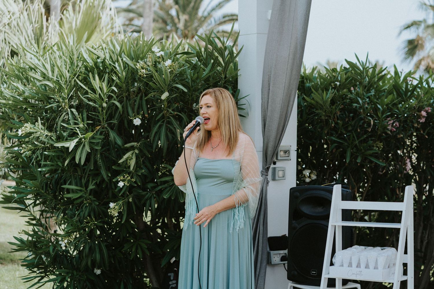 Woman in a sage green dress performs at an outdoor wedding venue.