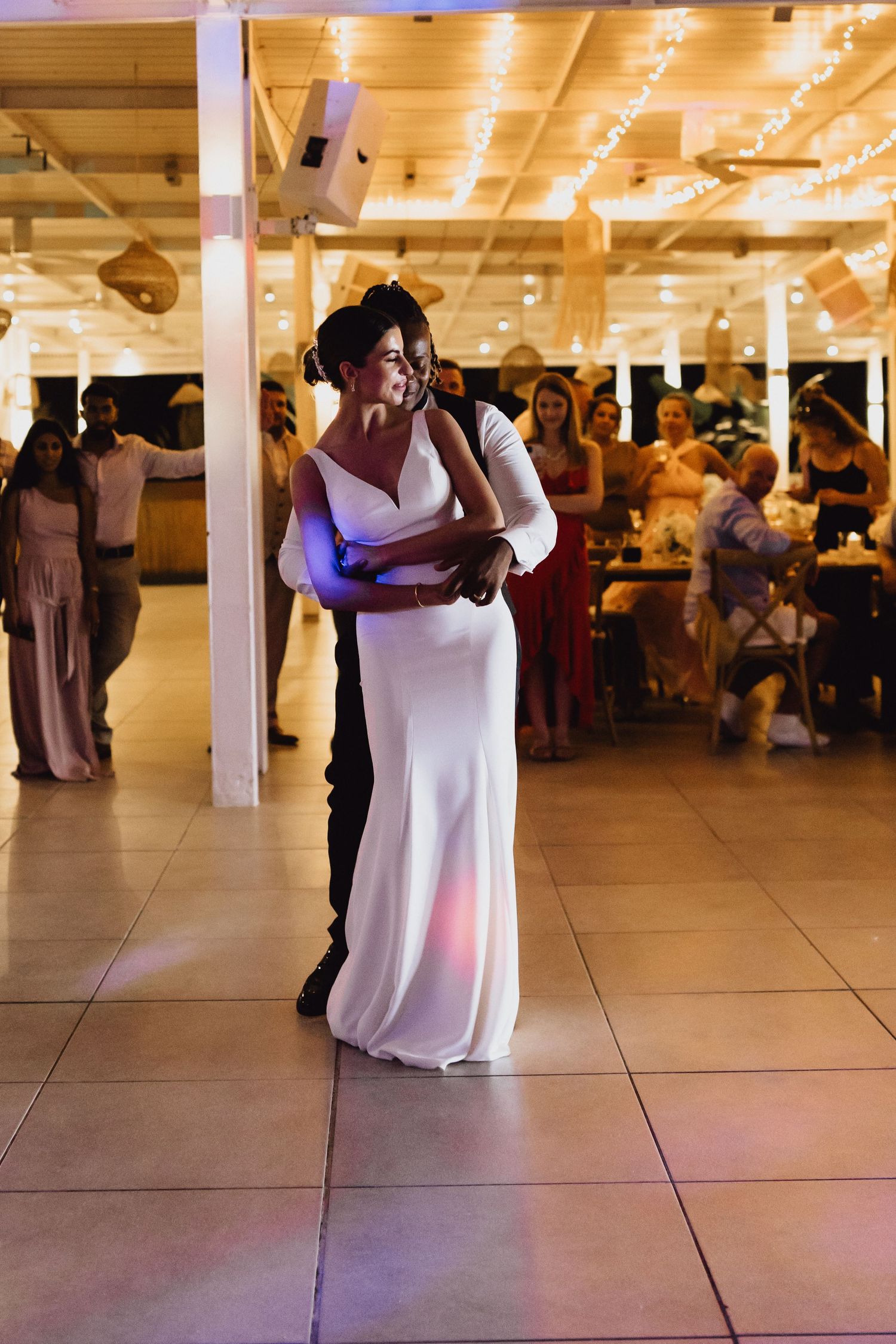 Wedding reception first dance captured under warm string lights and industrial ceiling.