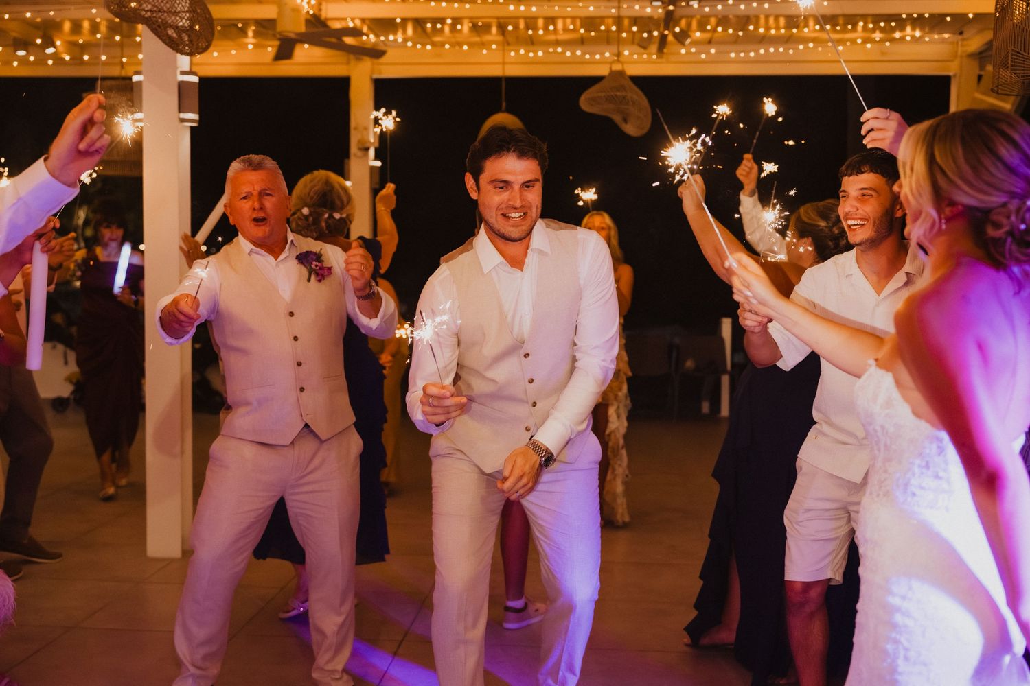 Wedding party dancing and celebrating under string lights at an evening reception.