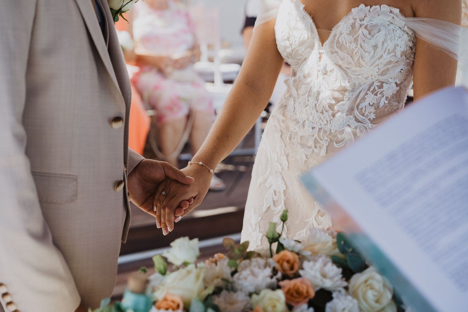 Close-up details of a lace wedding dress and bouquet at a beach ceremony.