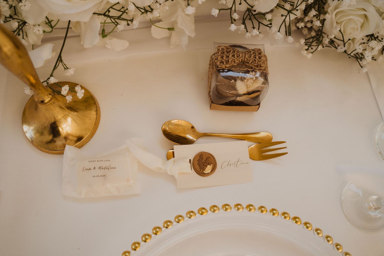 Gold fork and spoon beside a wax seal place card and wicker favor box on a beaded charger plate.