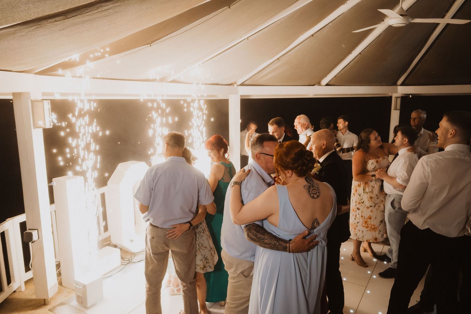 Wedding guests dance together under fairy lights inside a tent at an elegant evening wedding reception.