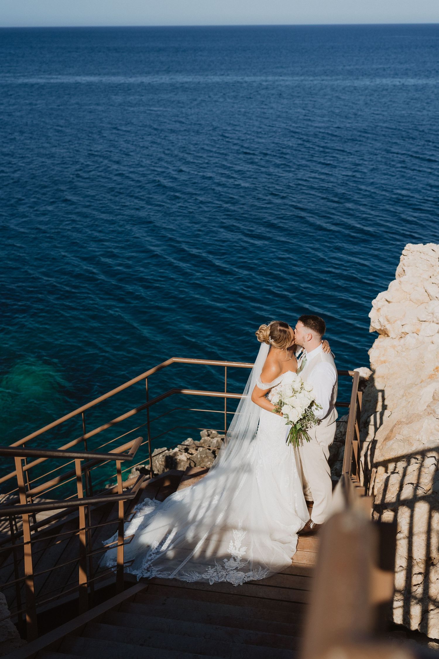 A couple shares a romantic moment on a seaside terrace overlooking deep blue Mediterranean waters.