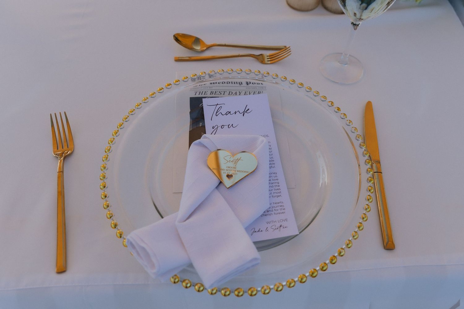 Elegant gold-rimmed place settings with white napkins and gold utensils arranged on a light tablecloth.