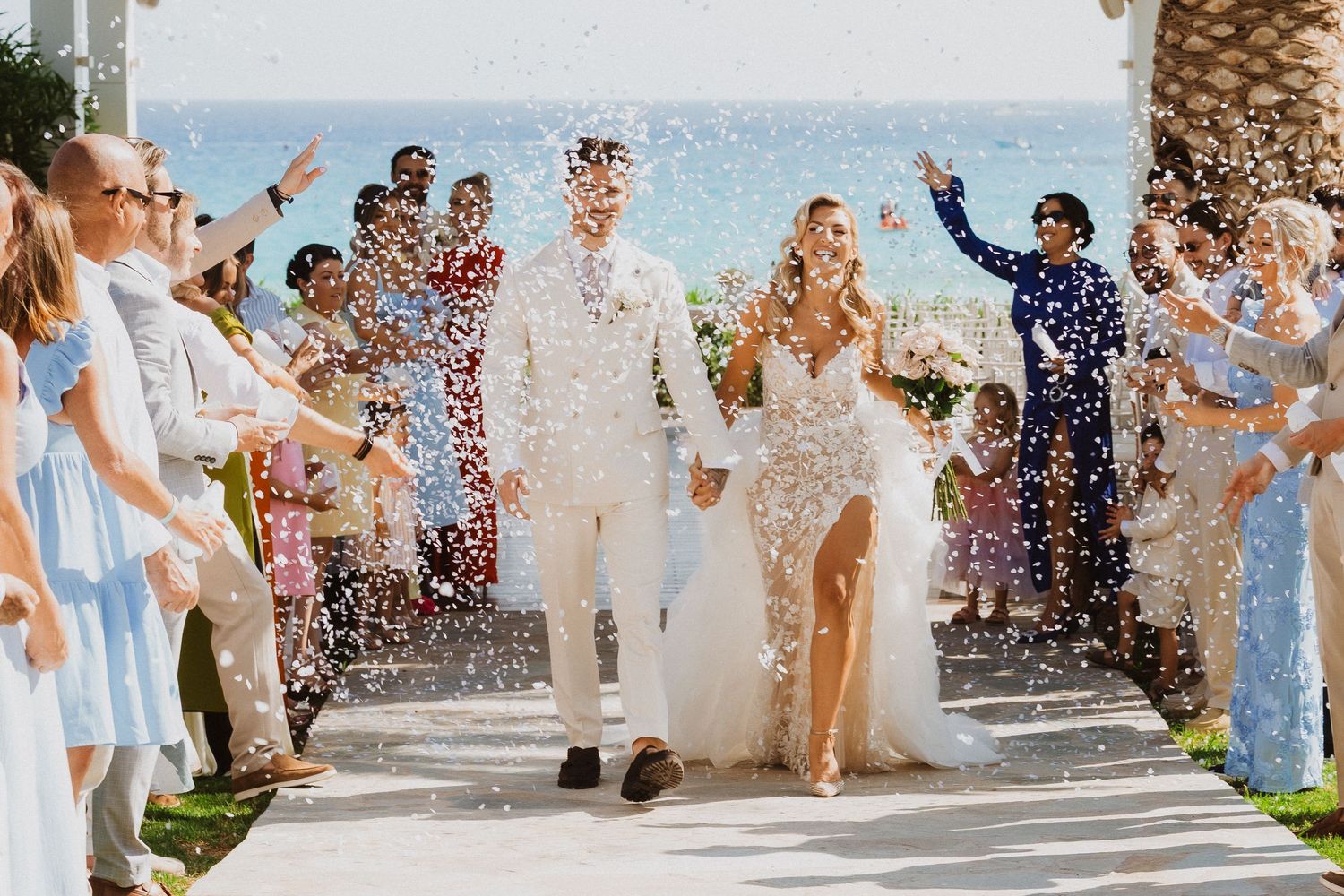 Wedding guests toss confetti and celebrate as a couple exits down outdoor steps at a joyous celebration.