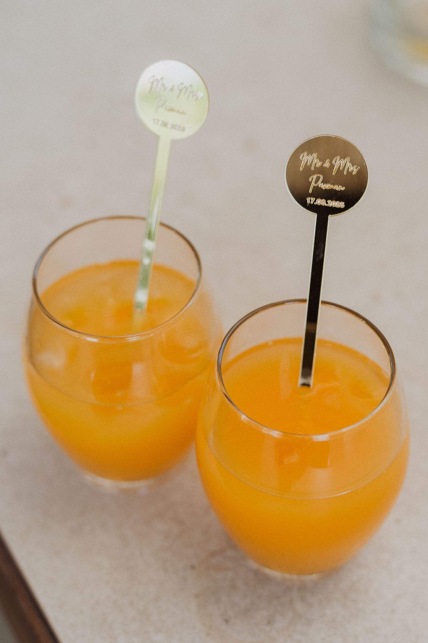 Two orange mimosa cocktails in stemless glasses with decorative drink stirrers marked 'Mr & Mrs' in brown and mint green.