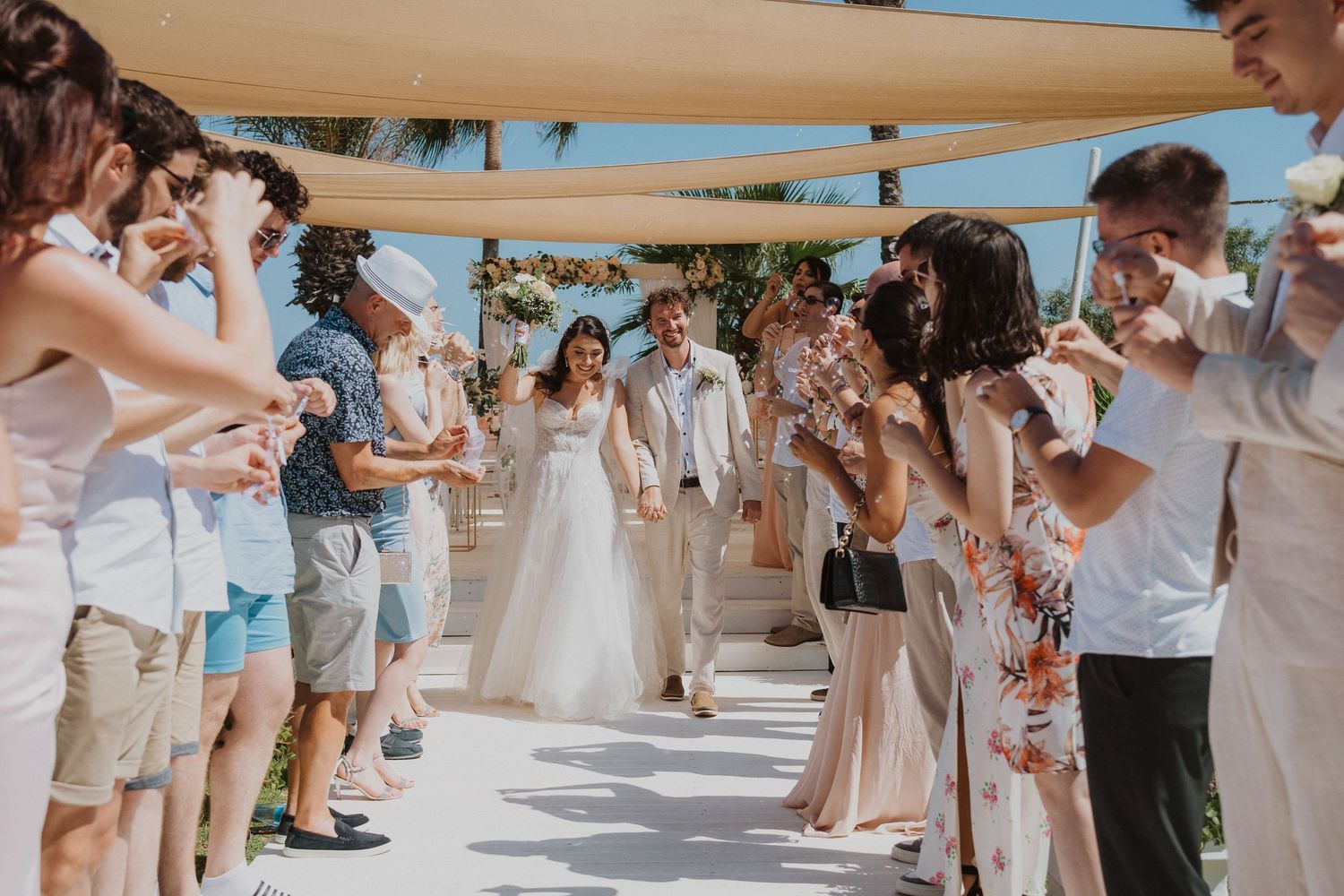Wedding guests create bubble-filled aisle for couple at outdoor beach ceremony.