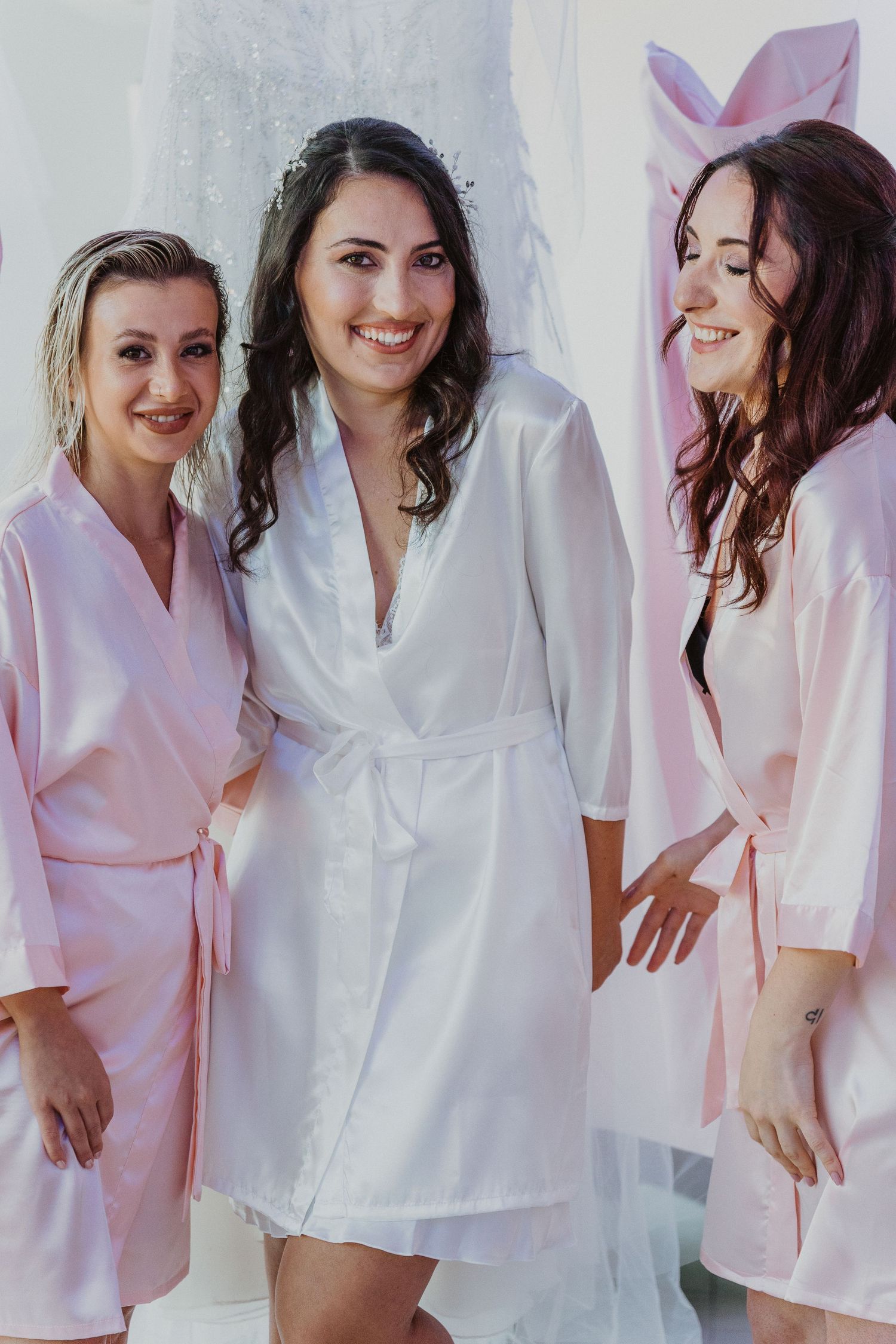 Wedding party poses playfully in matching satin robes with the bride in white and bridesmaids in pink.