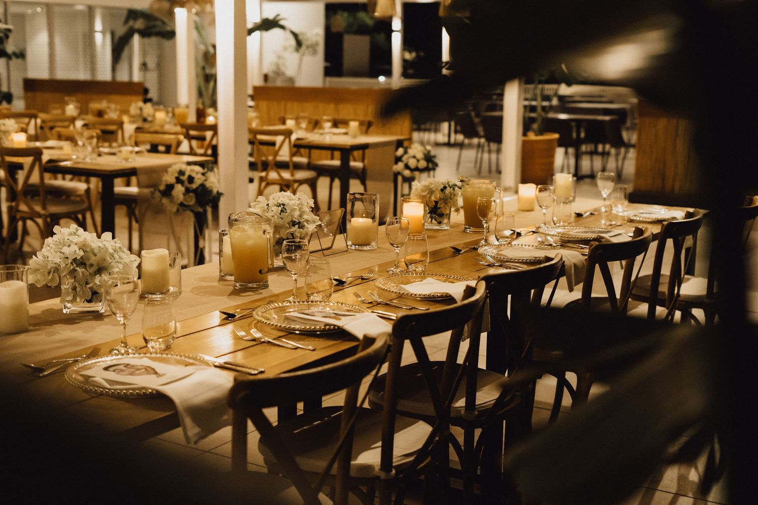 Romantic wedding reception table with vintage chairs and candlelit place settings.