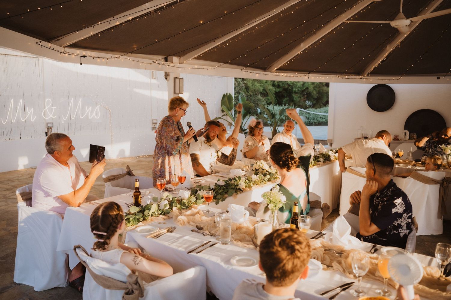 Wedding reception celebration with guests applauding during speeches at decorated dinner tables.