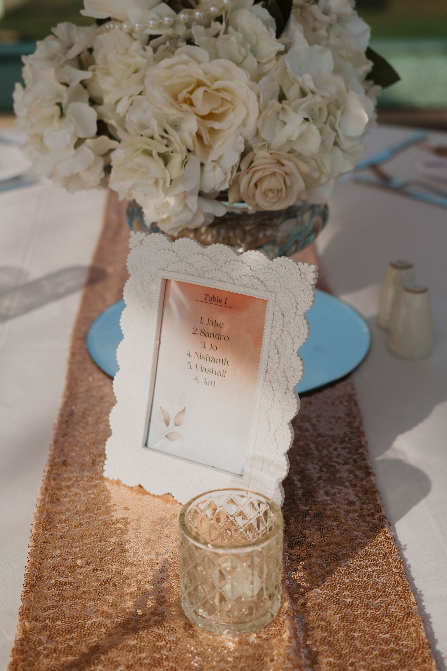 White roses centerpiece with ornate frame and sequined table runner at wedding reception.