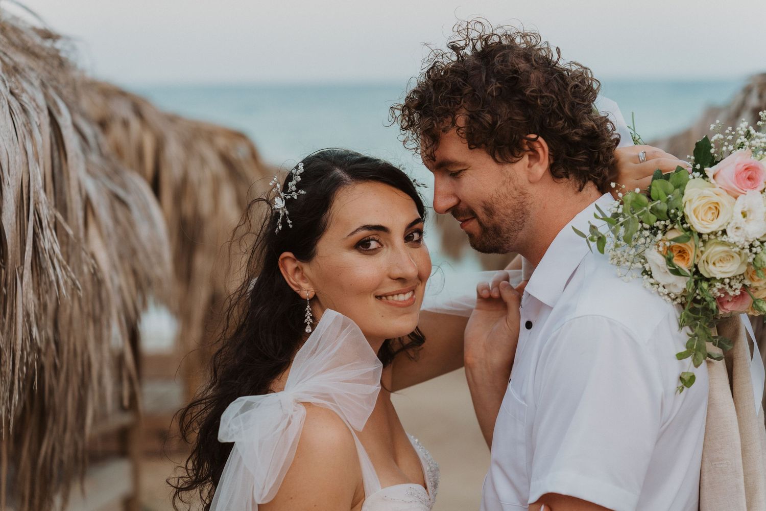 Close-up wedding portrait with floral bouquet against beachfront background.