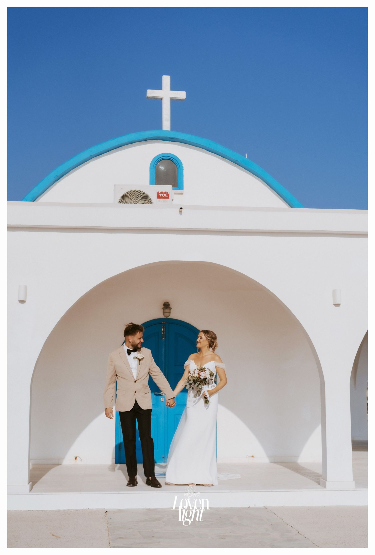Greek Orthodox chapel with white walls, blue dome and cross against bright sky.
