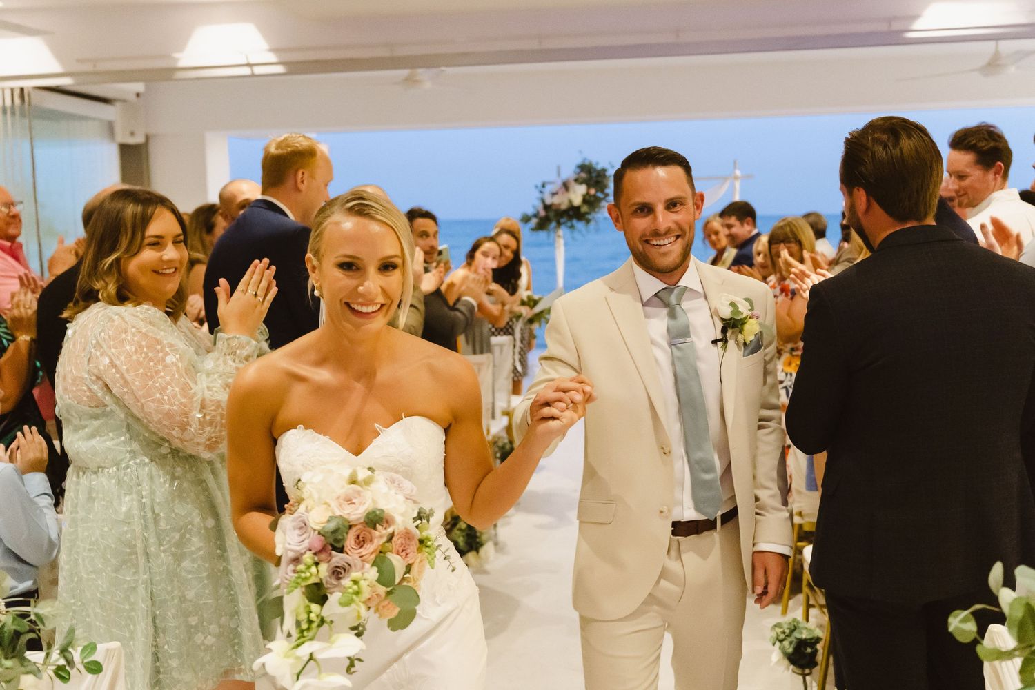 Joyful wedding exit with couple walking through crowd of applauding guests in bright venue.