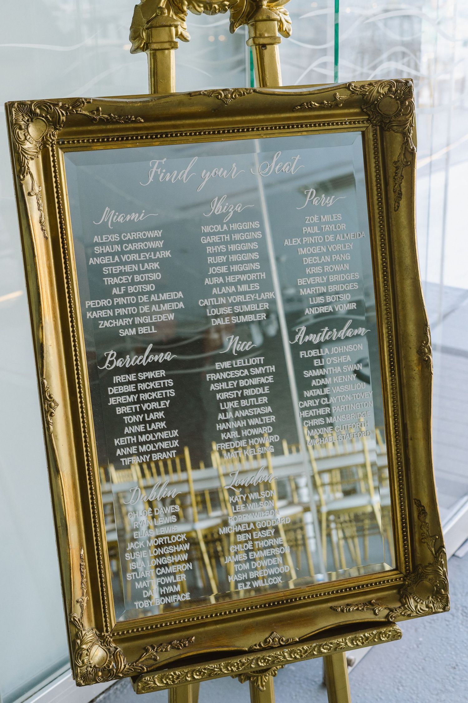 Vintage gold mirror with wedding table seating chart displaying guest names and table numbers.