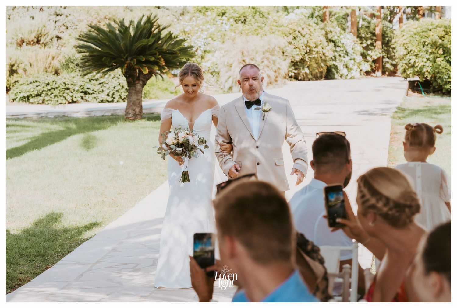 Wedding ceremony processional on outdoor garden path with palm trees.