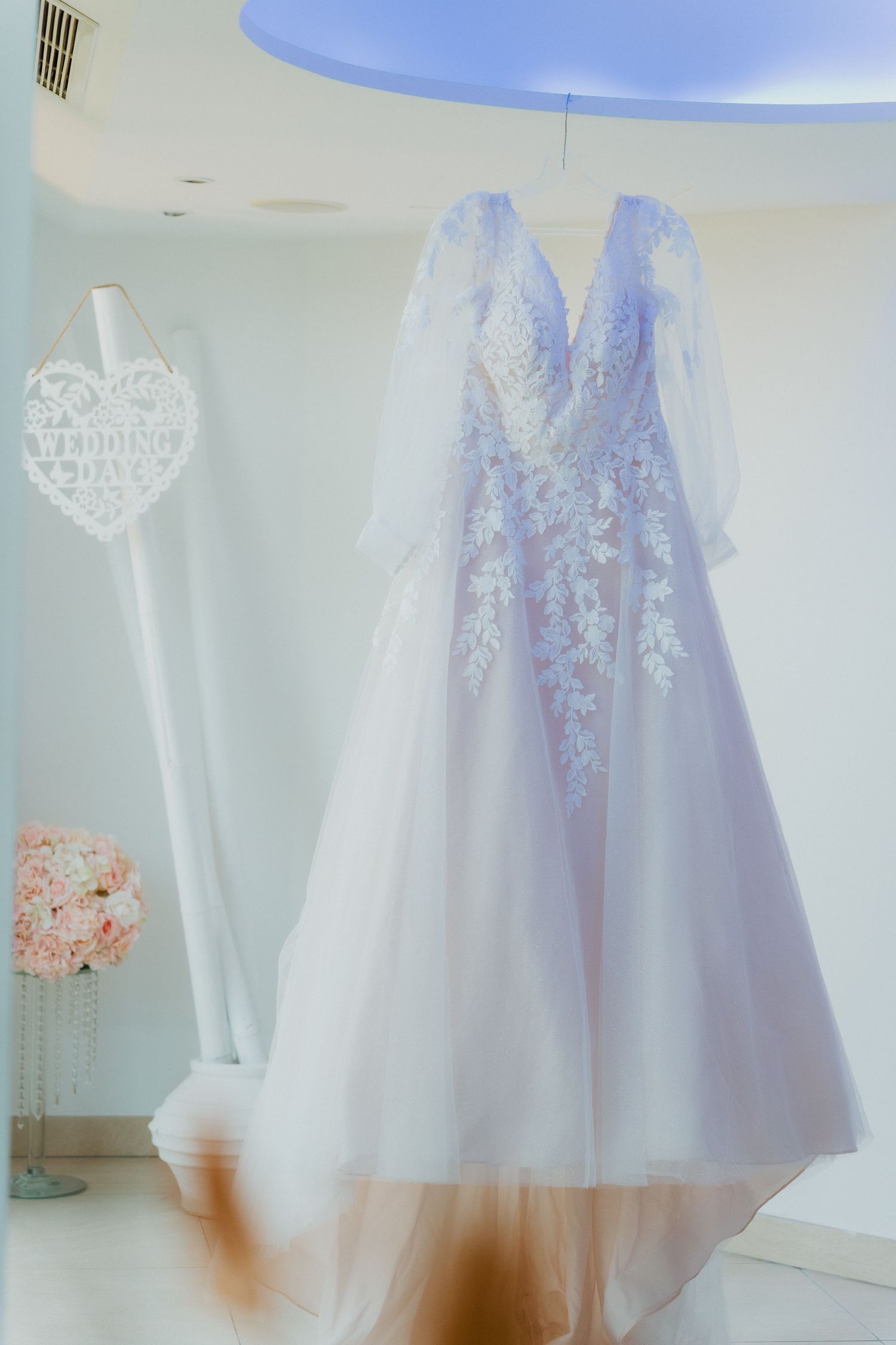 Elegant white lace wedding dress with floral appliques hanging in a bridal suite.
