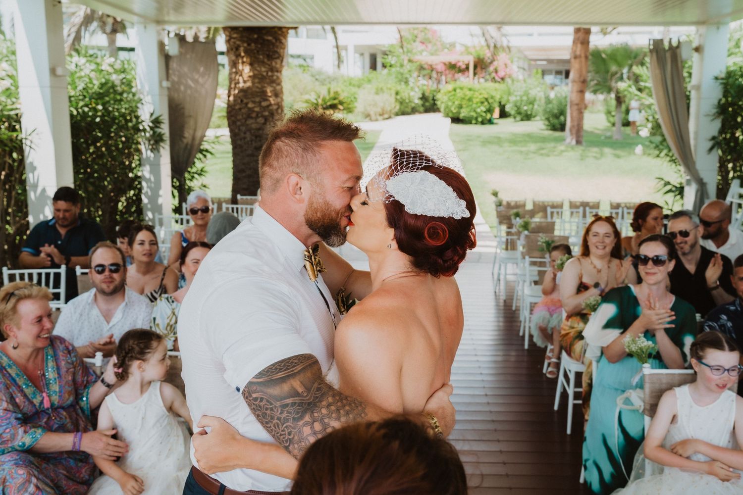 Newlyweds celebrate during their outdoor ceremony while guests look on from white chairs.