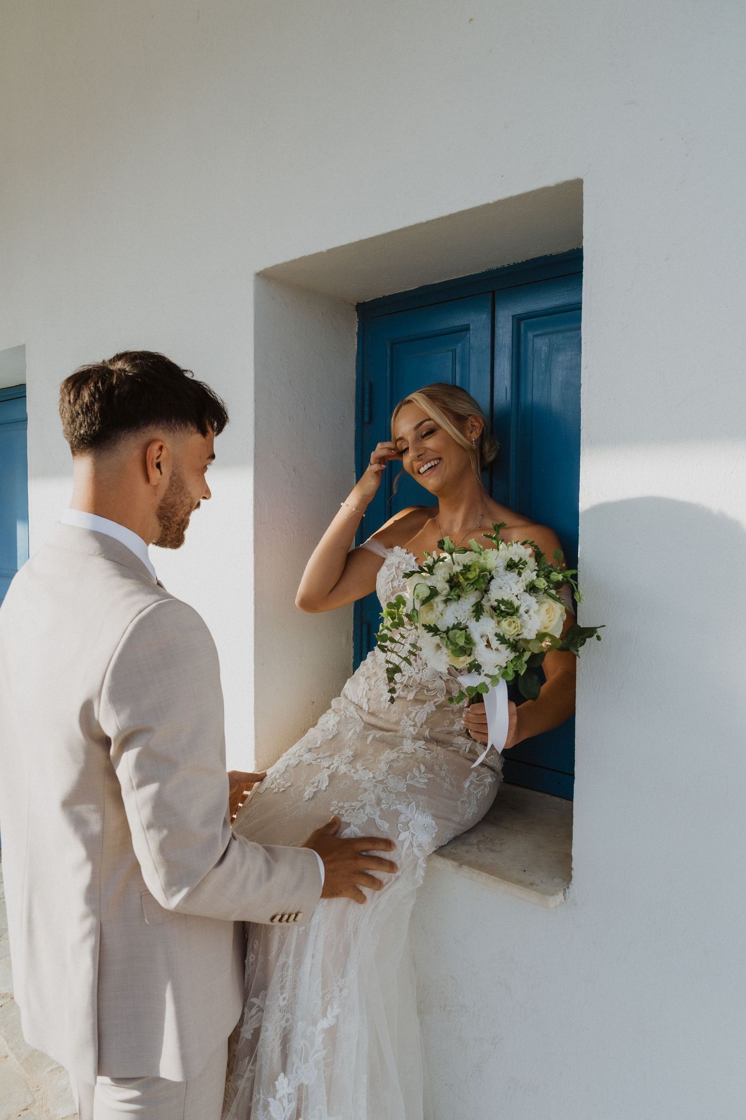 Playful wedding couple interaction in white Mediterranean building hallway.