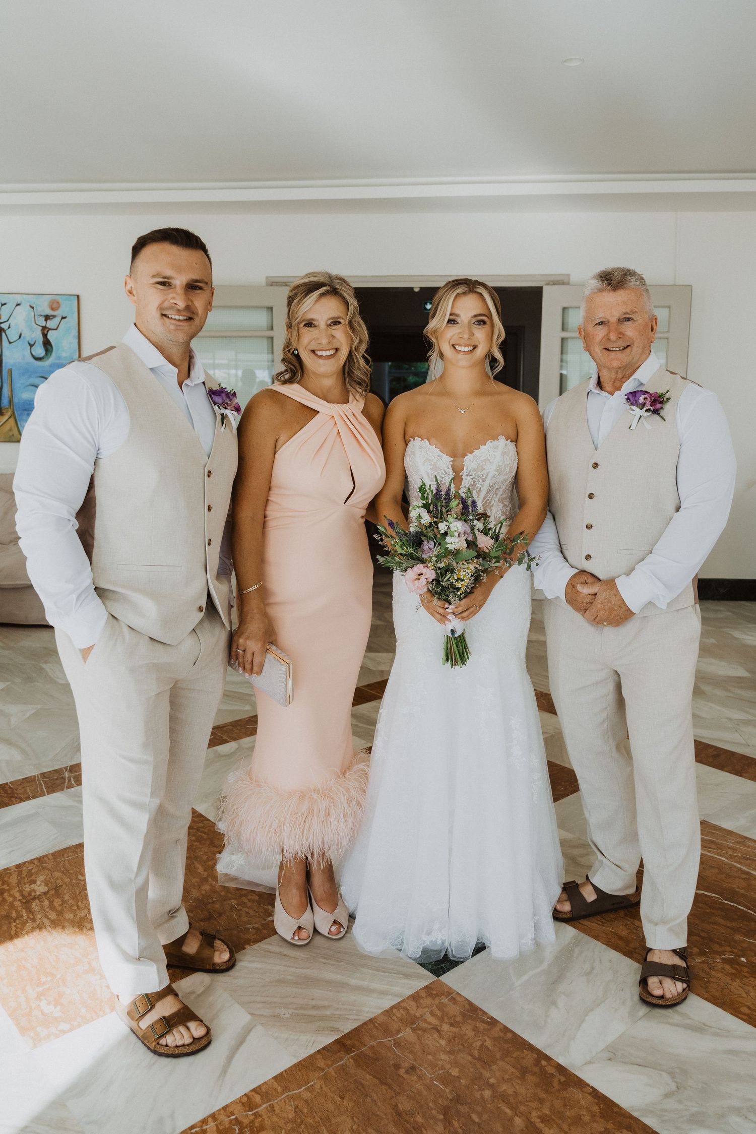 Wedding group photo featuring bridesmaids in peach dresses and groomsmen in light colored suits.
