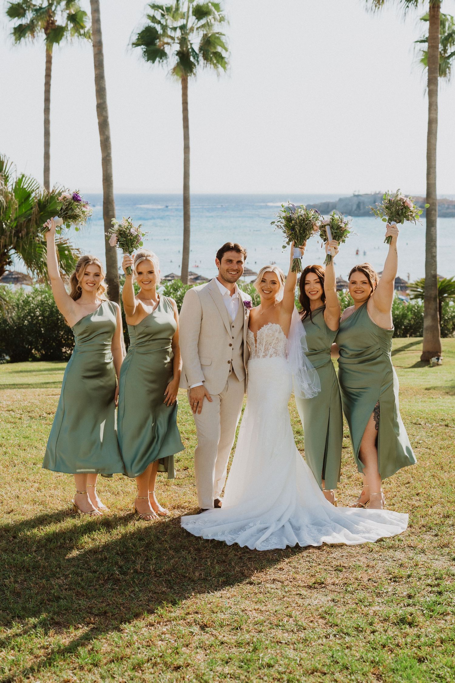 Wedding party in sage green and white attire posing for photos by the ocean.
