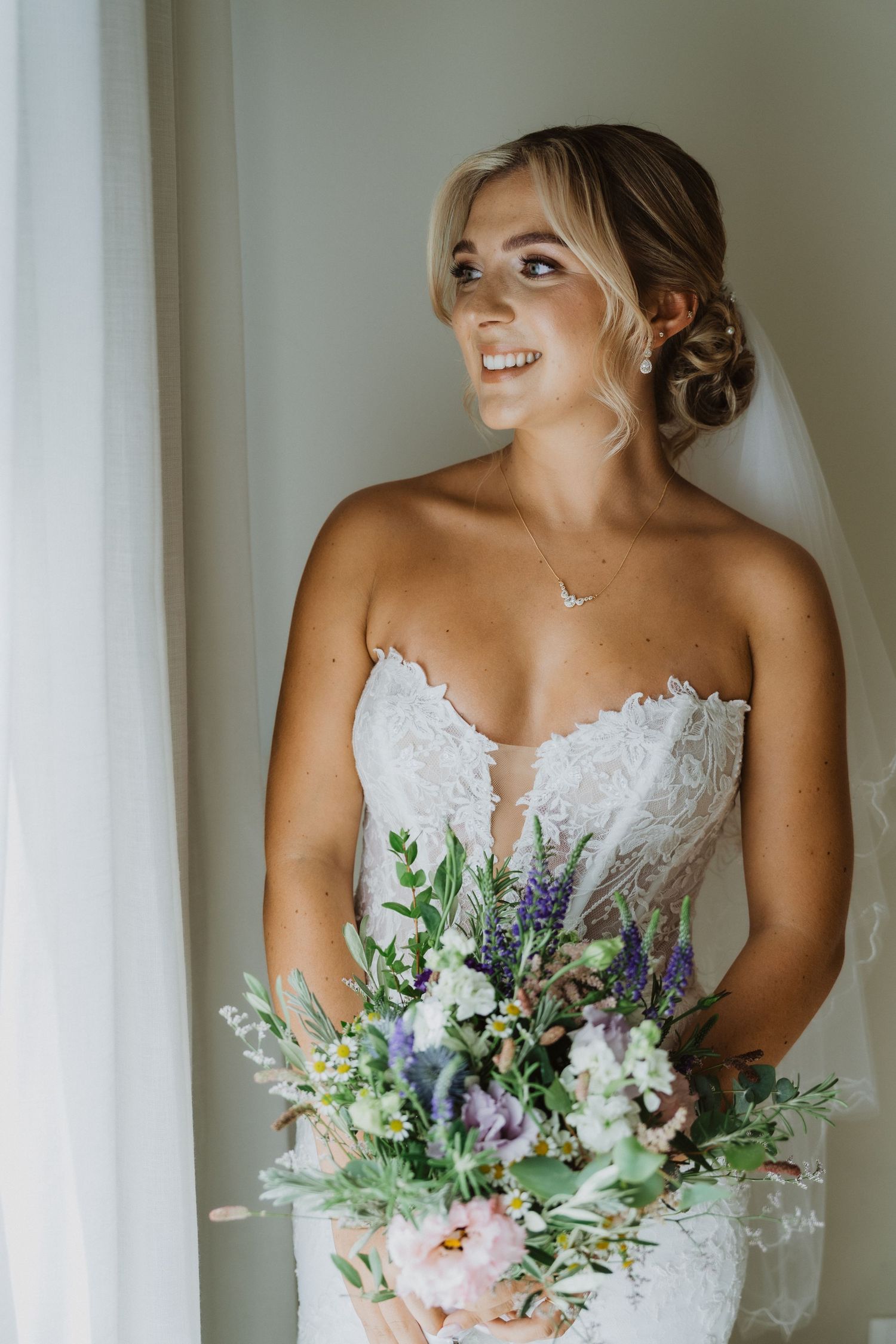 Natural light portrait of bride with delicate bouquet featuring lavender and white blooms.