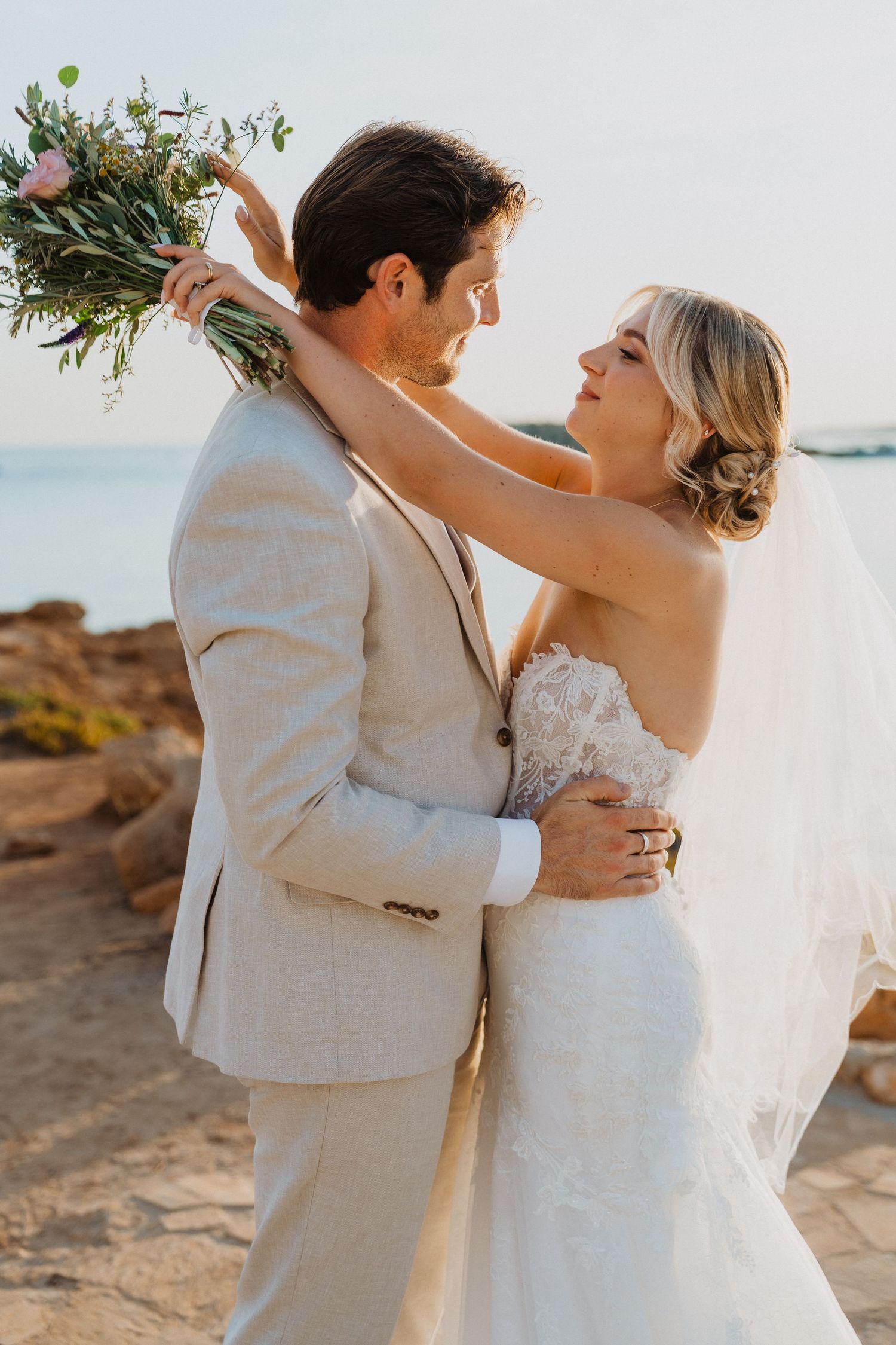 Romantic coastal wedding photoshoot with flowing veil and natural bouquet.