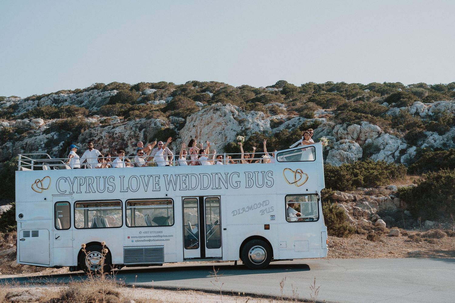 Cyprus Love Wedding Bus parked on a hill against a rocky landscape backdrop.