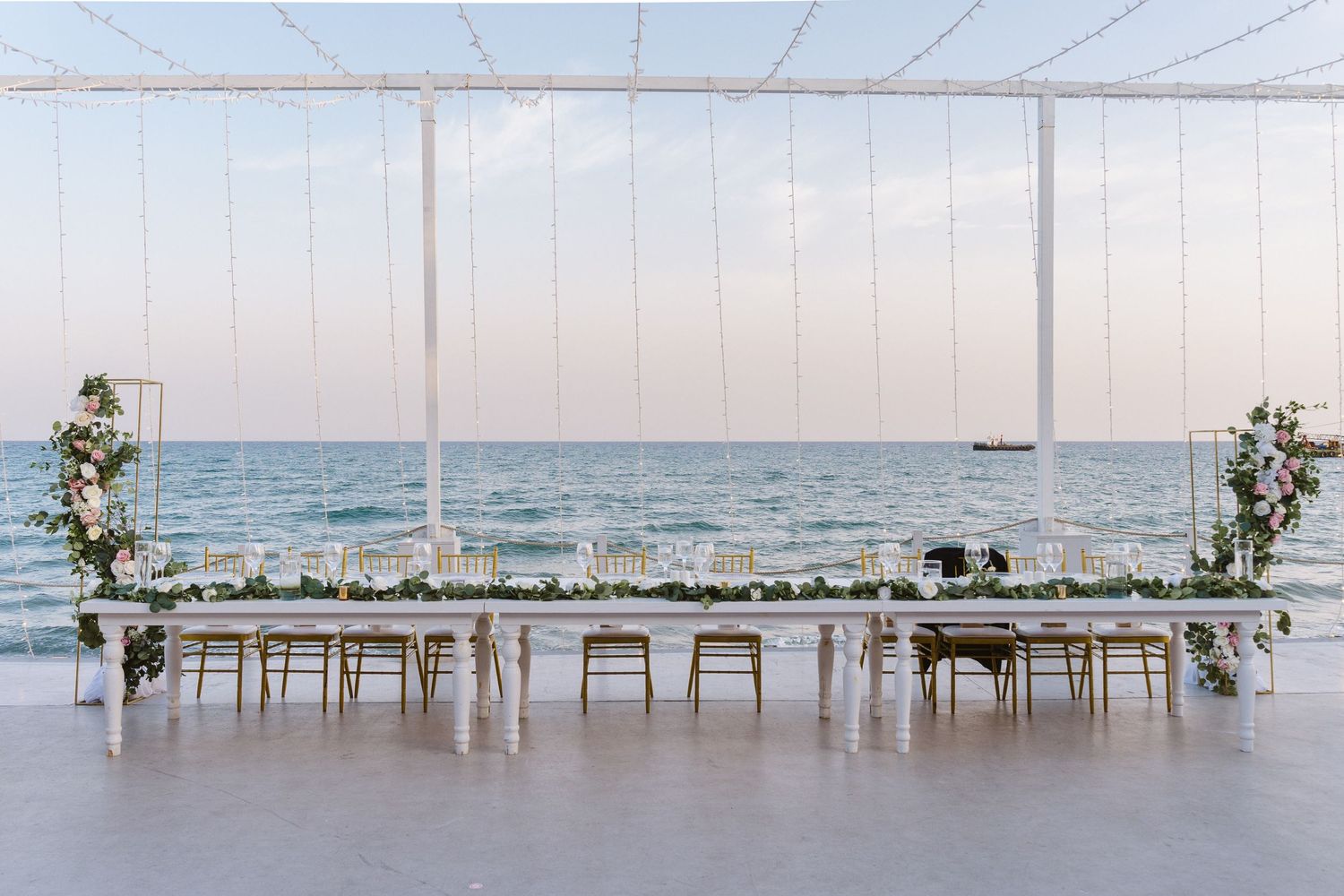 Minimalist waterfront wedding reception setup with white tables and chairs facing the ocean view.