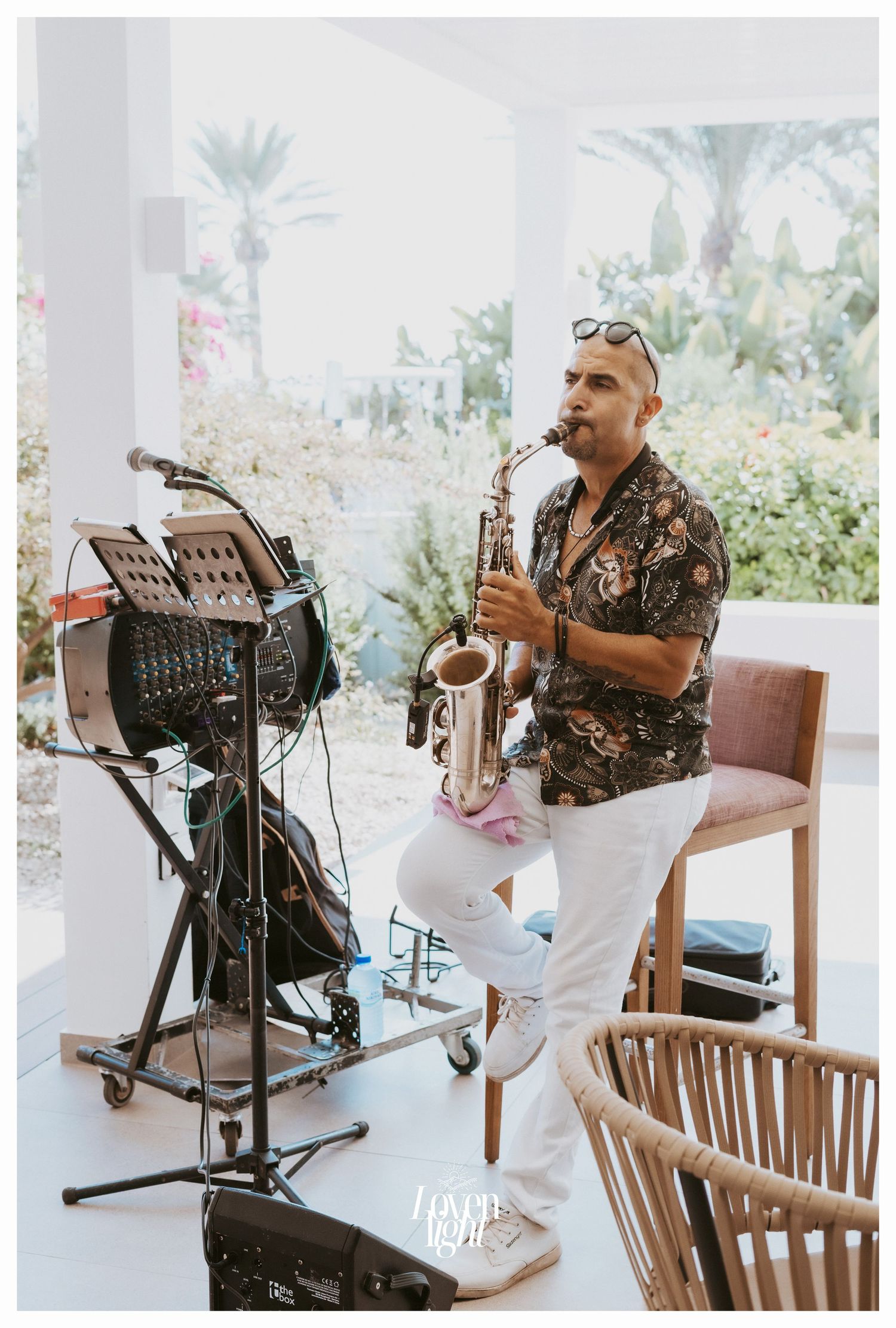 Musician playing saxophone at an outdoor venue with palm trees in the background.