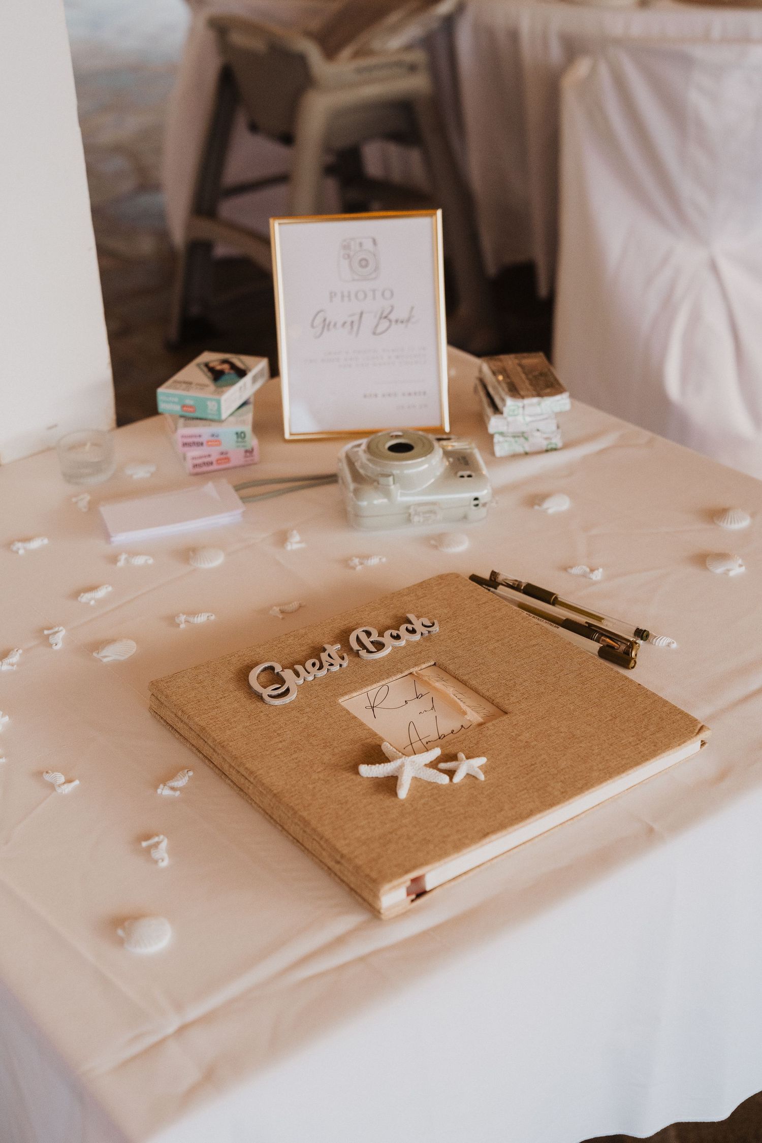 A wedding guest book and vintage camera displayed on a white tablecloth with delicate scattered confetti decorations.