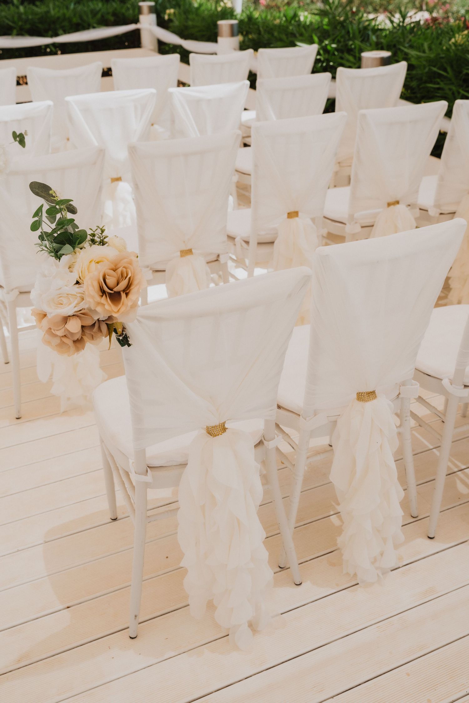 White wedding ceremony chairs decorated with cream flowers and flowing fabric sashes.