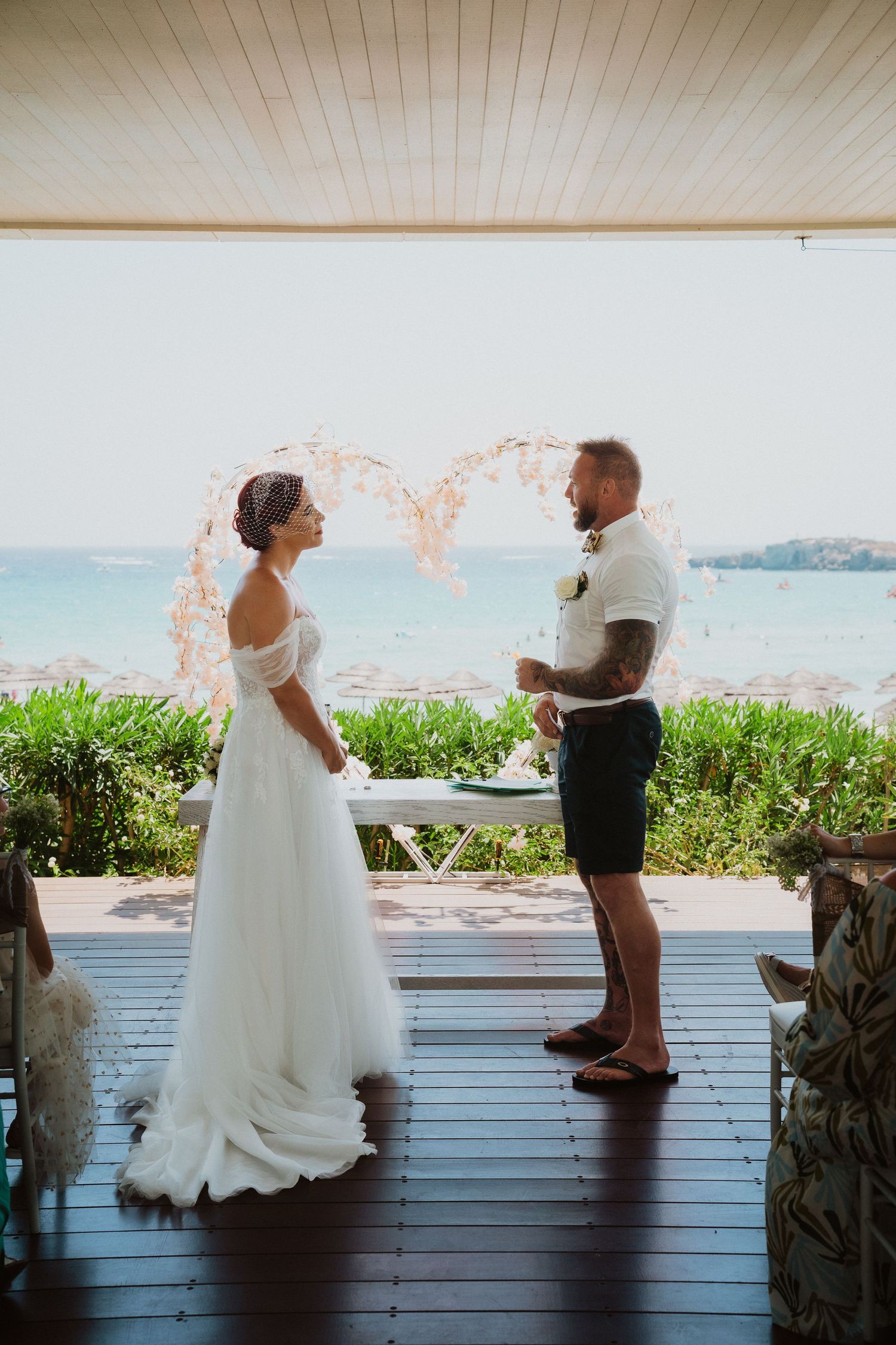 Beach wedding ceremony with white floral arch overlooking ocean view.