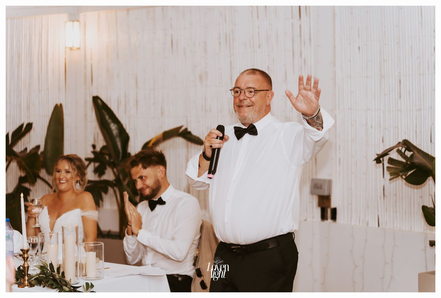 Speaker giving a toast at a wedding reception with microphone and bow tie.
