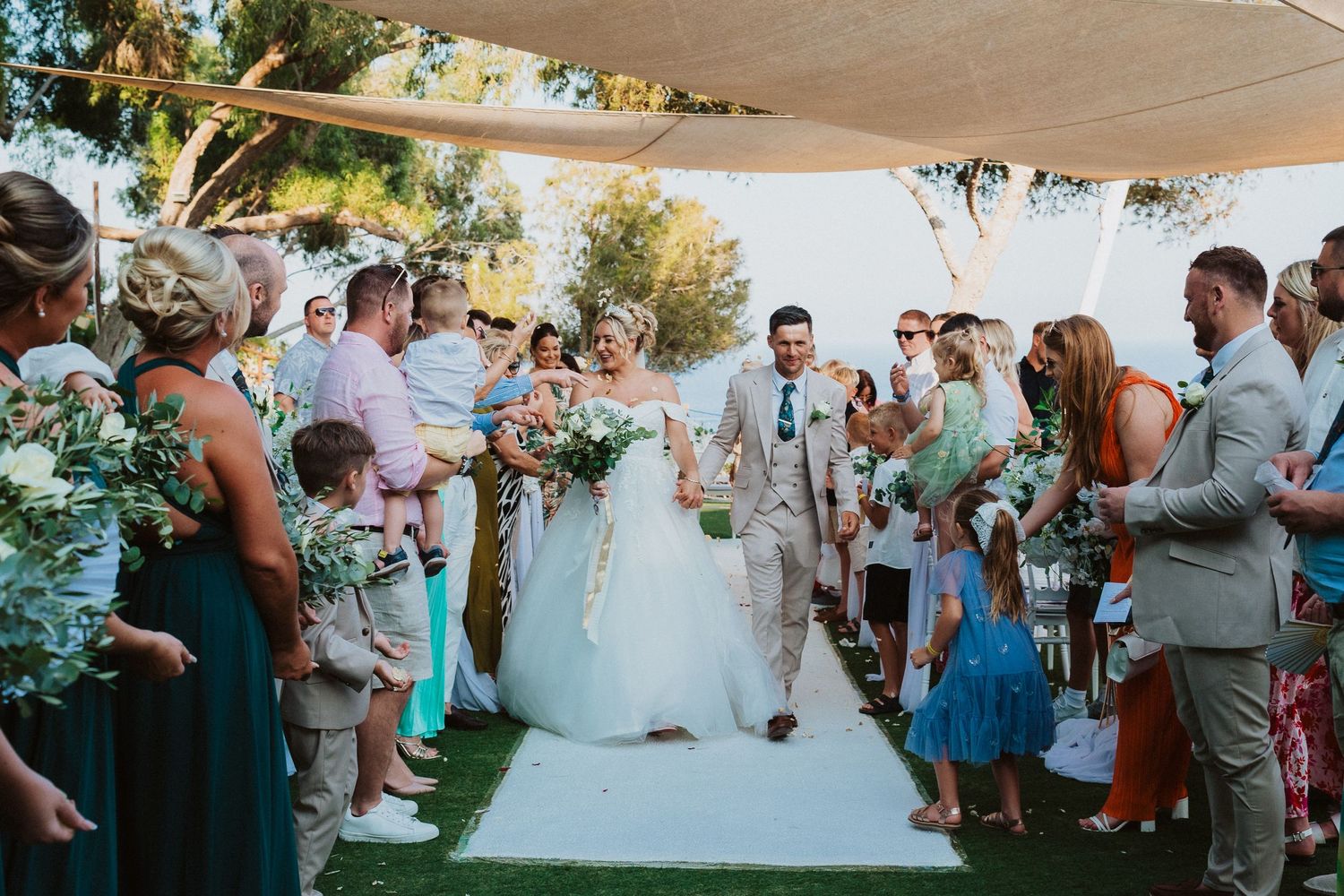 A joyful celebration takes place under an outdoor canopy with guests in mint and grey attire lining the white aisle.