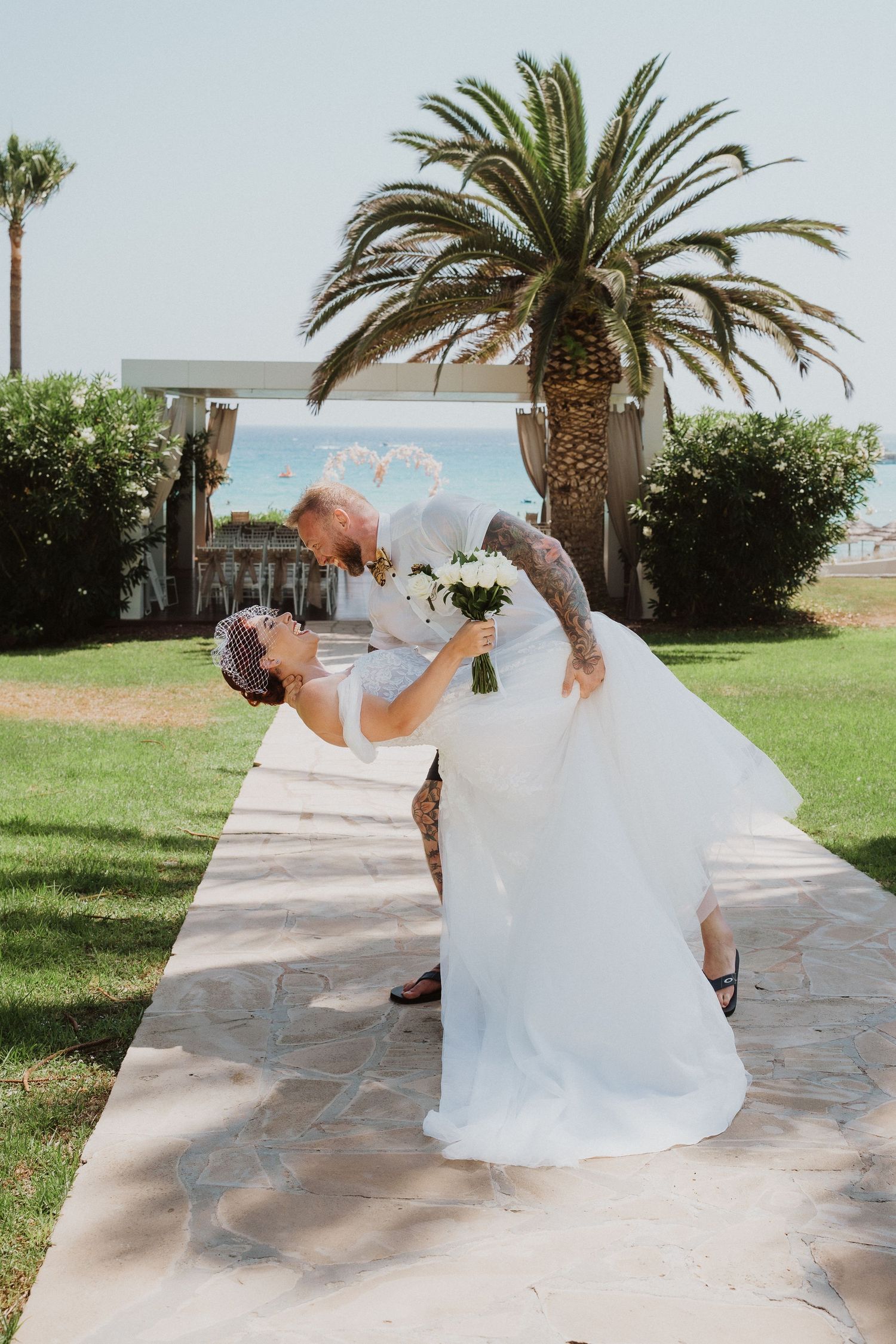 Romantic wedding couple dips in a playful dance move under a tropical palm tree.
