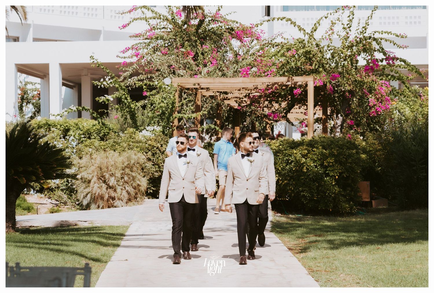 Wedding party walking through a garden path lined with flowering plants.