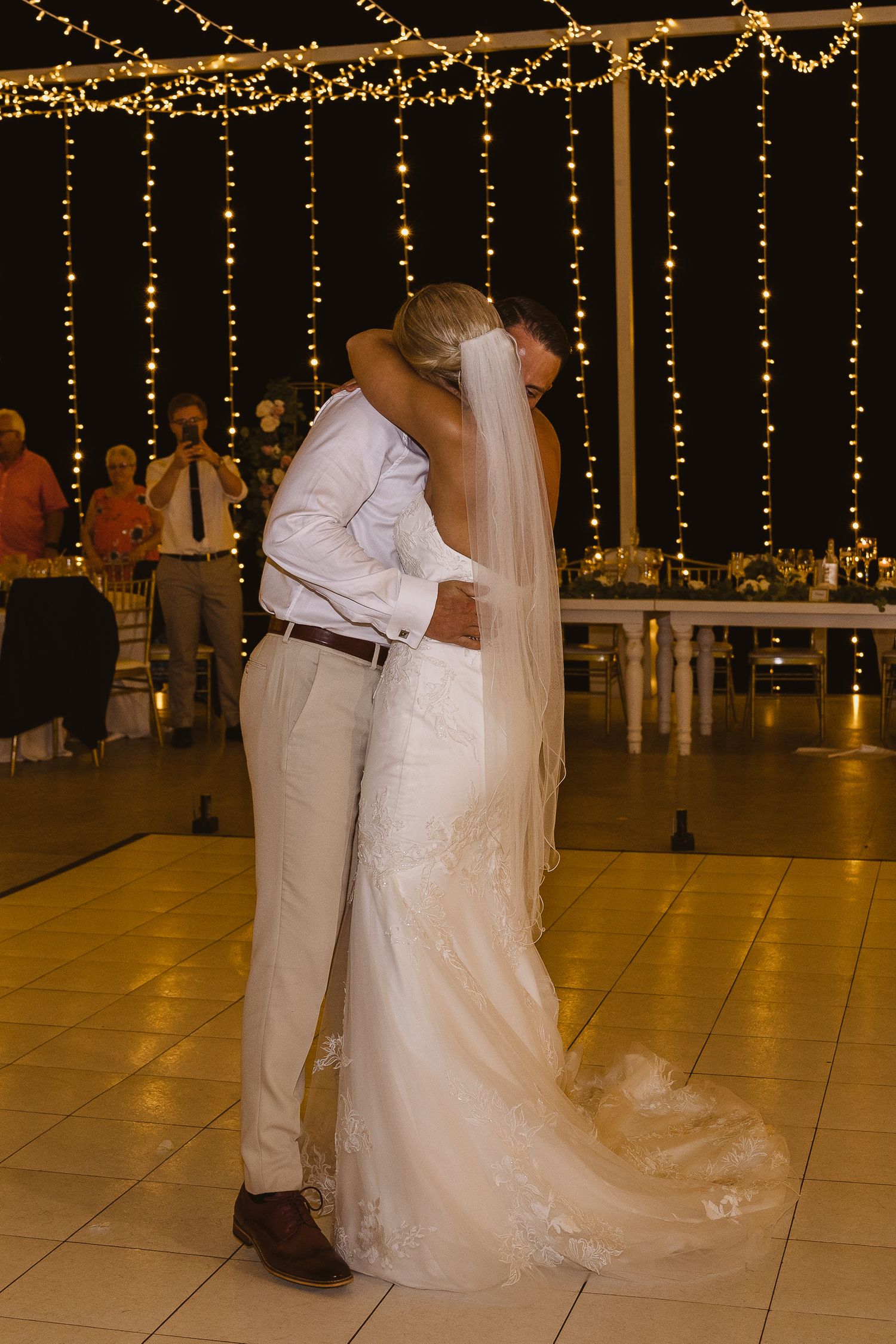 A couple shares their first dance under romantic string light decorations at their wedding reception.