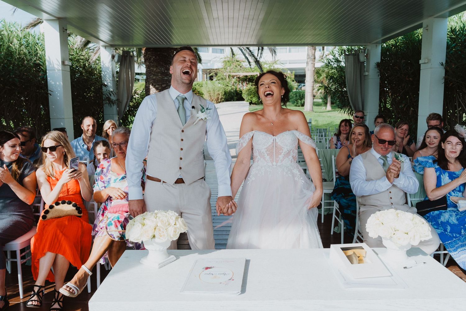 Happy newlyweds share a joyful moment together during their outdoor ceremony while guests look on.