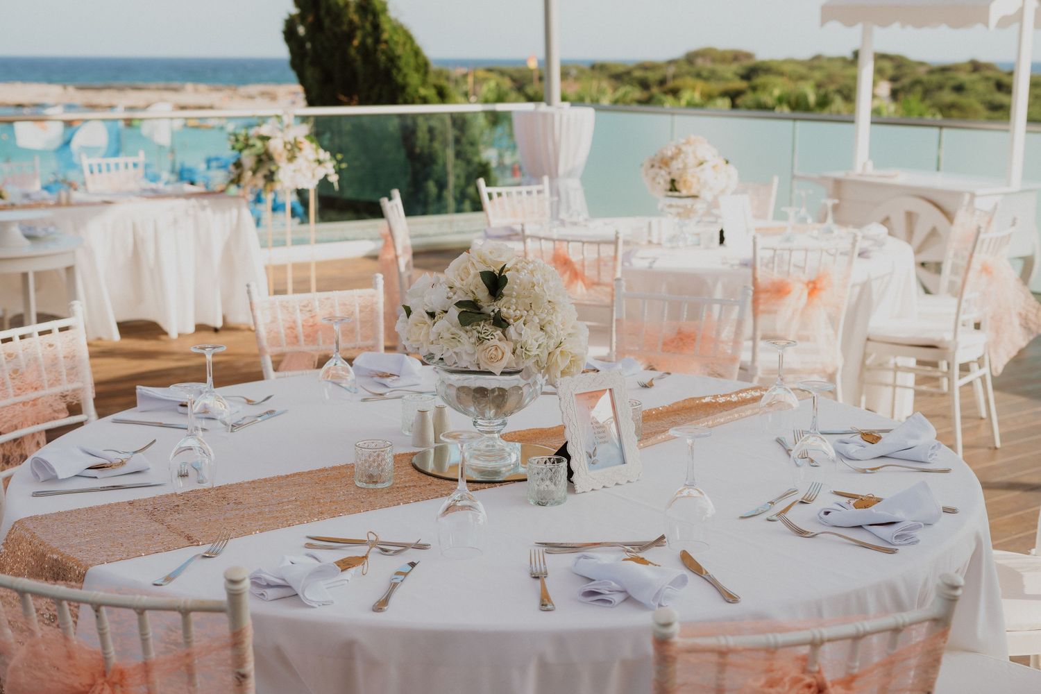 Elegant round table settings at an outdoor wedding reception with peach and white decor overlooking the ocean.