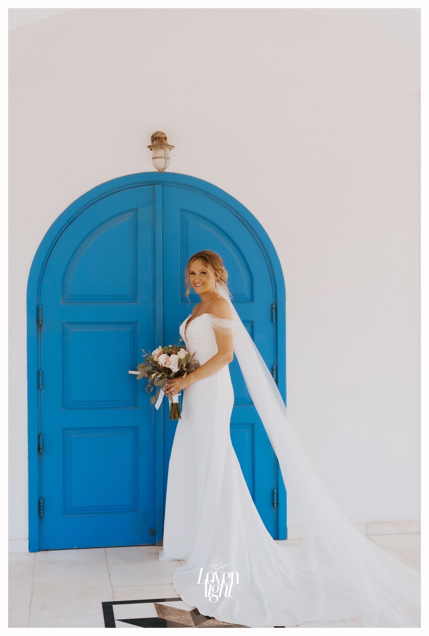 Solo bridal portrait featuring flowing white dress and bouquet against Mediterranean blue door.